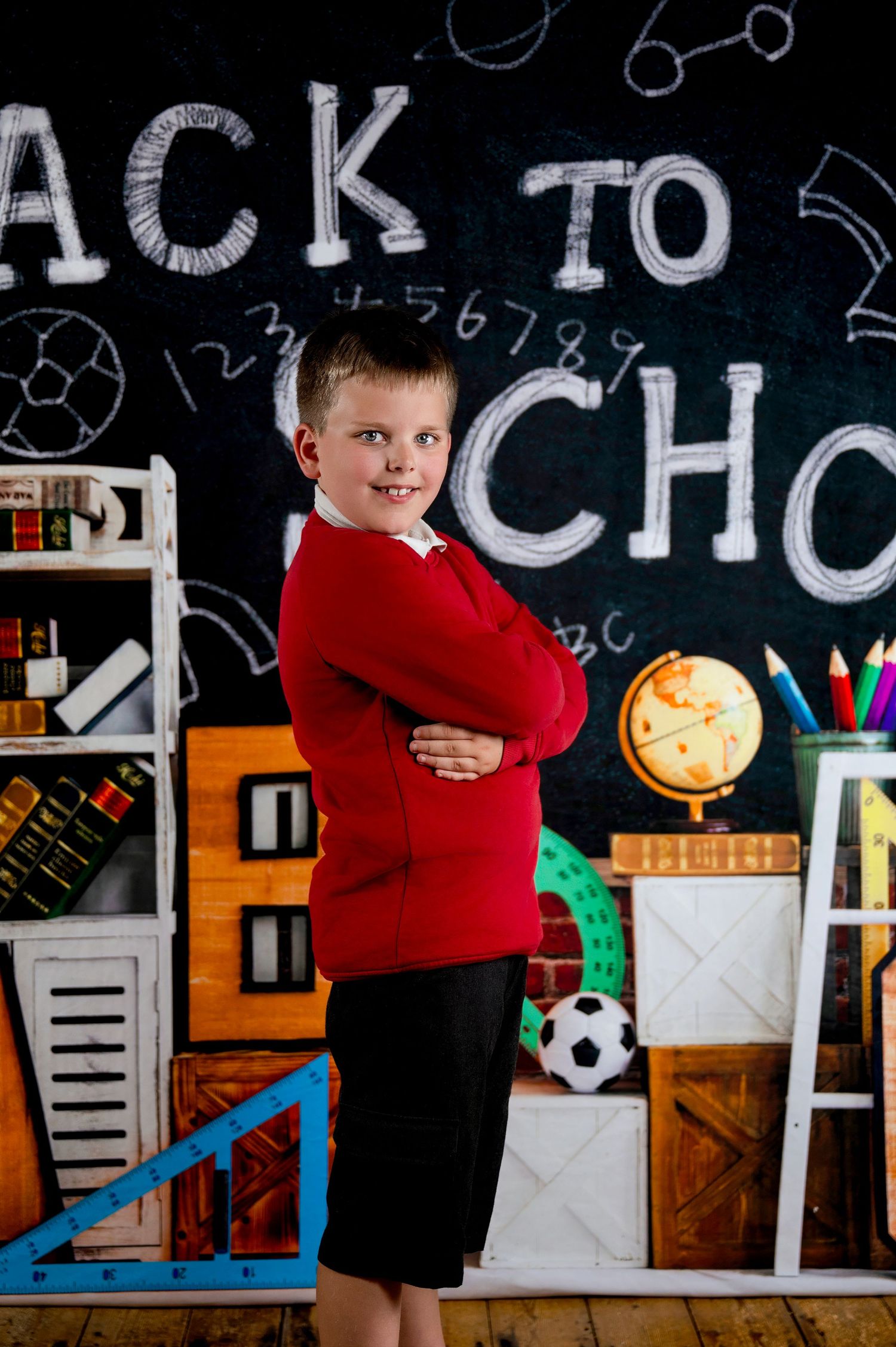 A student stands confidently in front of a back-to-school chalkboard display with school supplies and decorative elements.