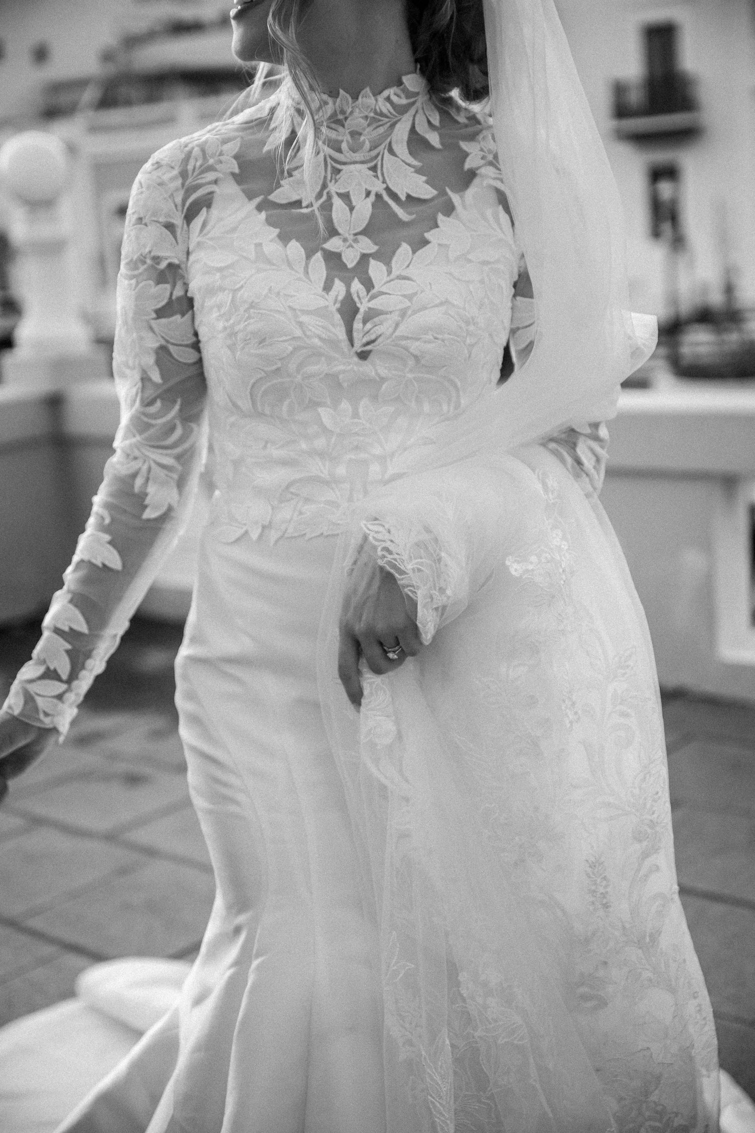 Close-up detail of a bride wearing an elegant lace wedding gown with long sleeves and high neckline in black and white.
