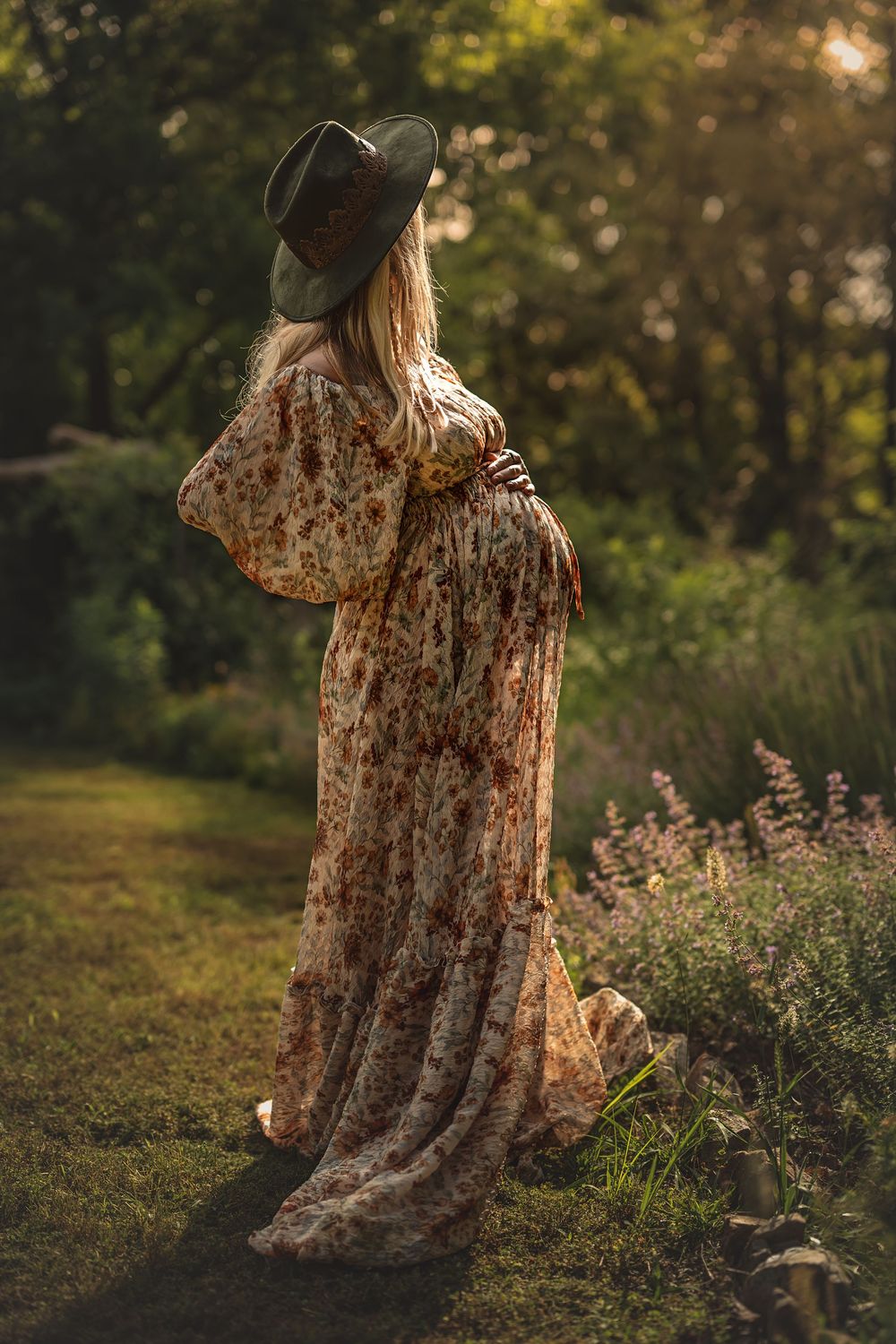 Backlit pregnant woman in a floral dress stands in a garden during golden hour for Lookout Mountain maternity photos.