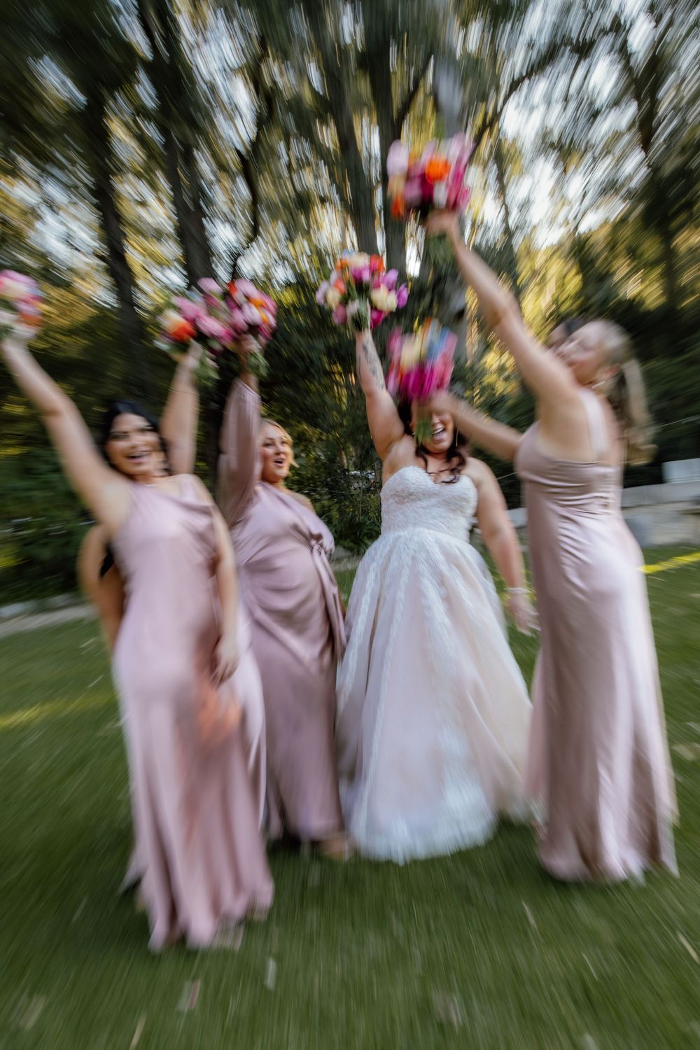 Motion-blurred sequence of bridesmaids in pink dresses and bride in white gown jumping and celebrating outdoors.