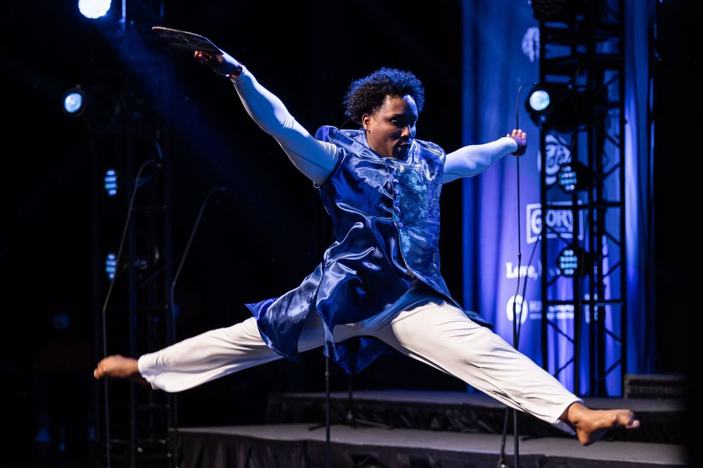 Dynamic dance performance featuring dramatic leaps and movements on stage under blue lighting.