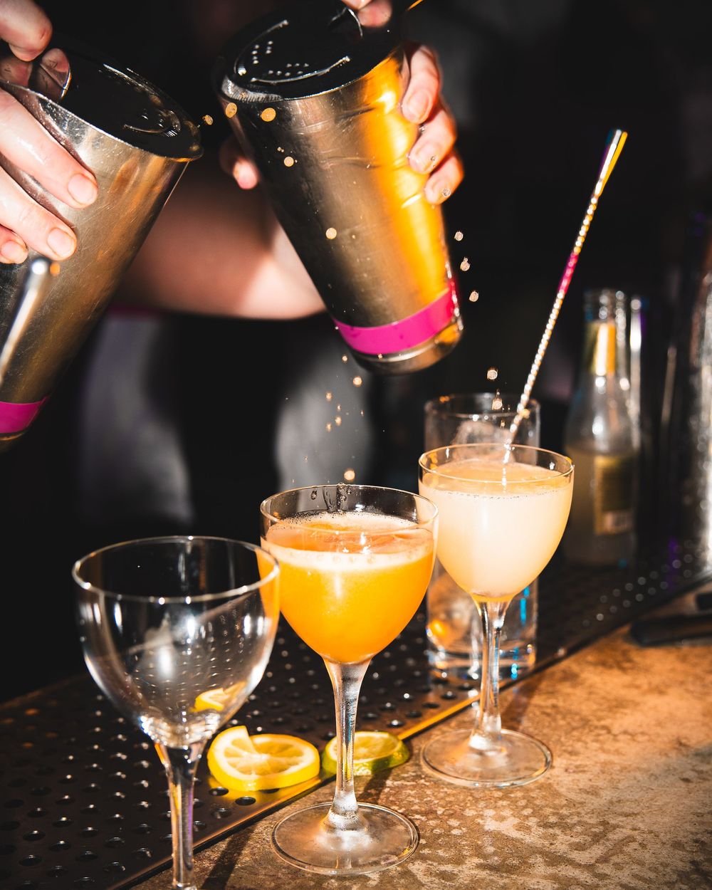 Mixologist pouring orange and cream-colored cocktails into martini glasses.