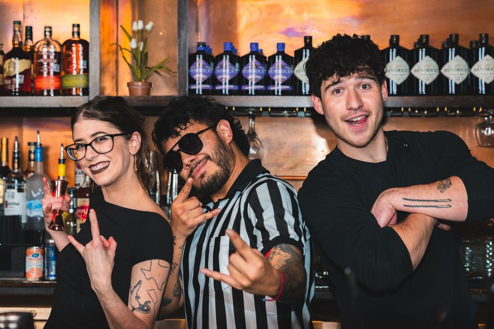 Bar staff posing together behind counter with bottles displayed on shelves.