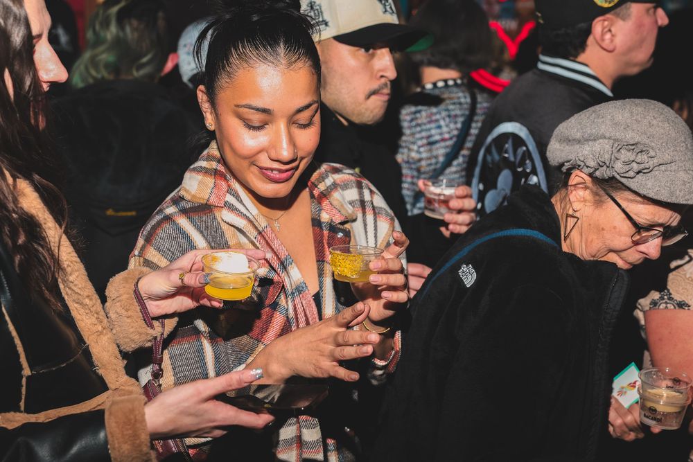Crowd of people holding and examining small tasting glasses at event.