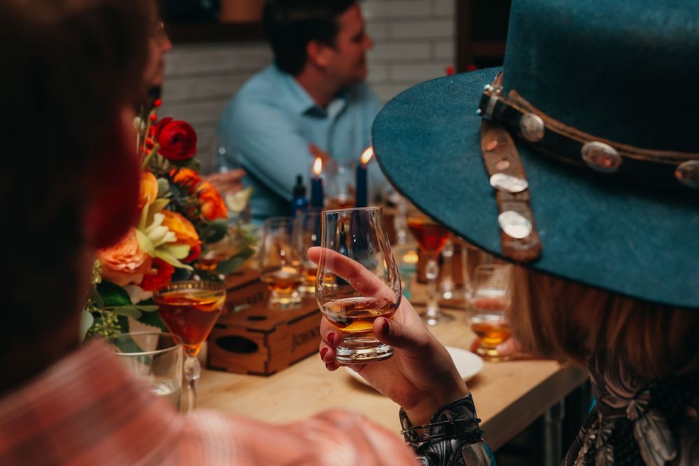 Close-up of hands holding cocktail glasses with blue hat in foreground.