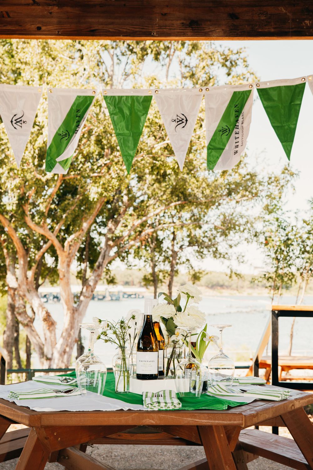Outdoor event space with wooden tables and green bunting flags hanging under trees.