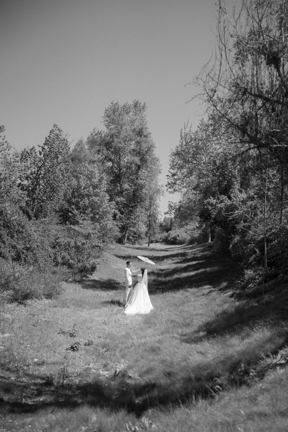 A flowing white wedding dress moves gracefully through a natural wooded landscape in black and white.