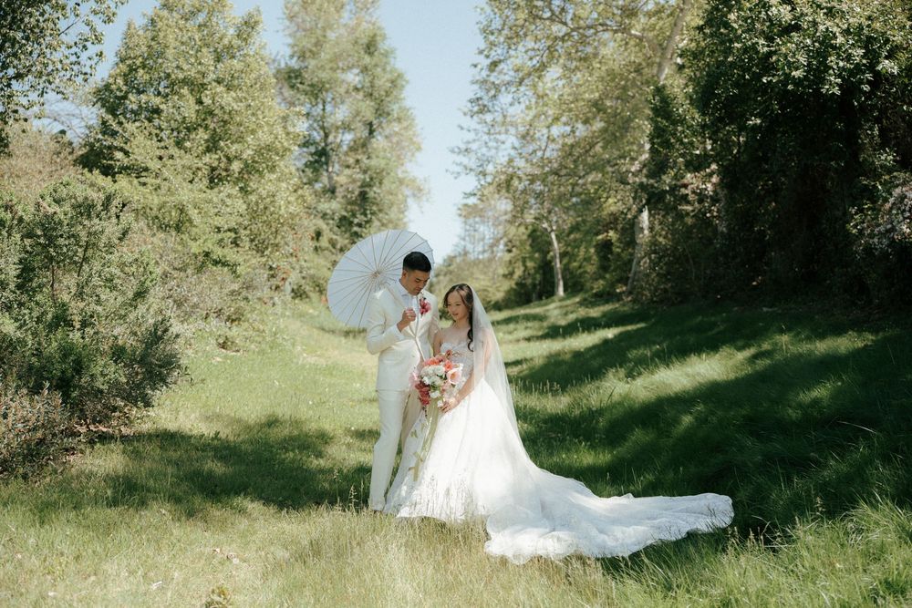 A couple embracing in a romantic outdoor wedding photoshoot among green trees on a sunny day.