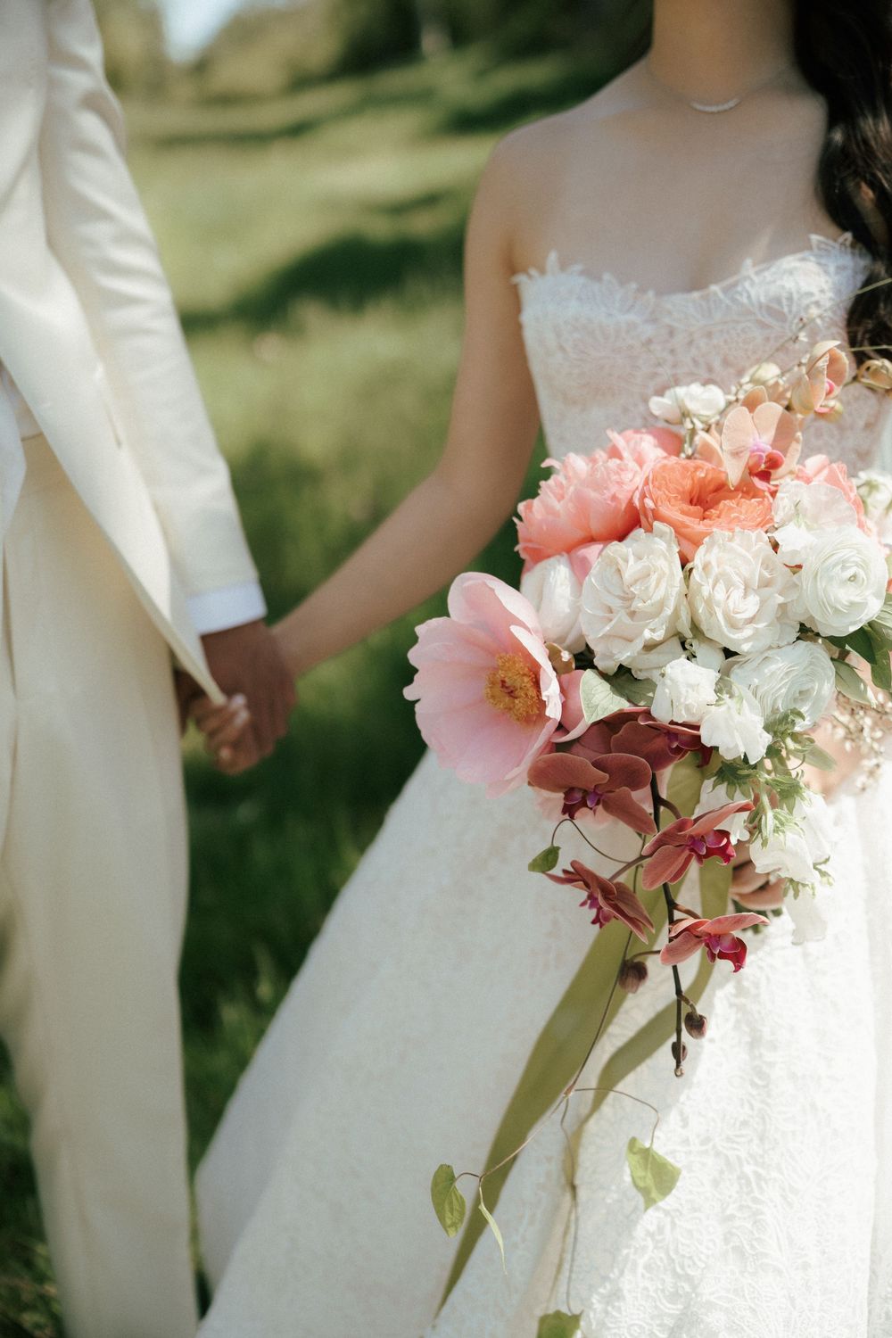 Dreamy close-up of delicate pink and white wedding bouquet with roses and trailing foliage against a white dress.
