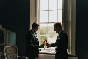 A candid wedding photo of groom and father standing near bright windows in a dimly lit room at Hirst Priory - taken by Grimsby photographer