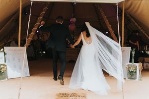 Newlywed couple enters reception tent with flowing veil and lanterns lining the path on their special day at Hirst Priory.