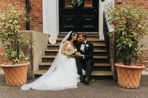 Formal wedding photos taken outside a historic brick building with elegant entrance stairs and potted plants at Hirst Priory.