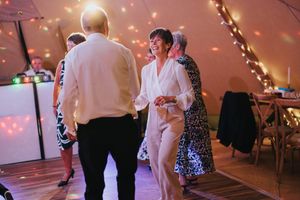 Wedding guests dance and mingle at a reception under warm string lights in an elegant tent-like venue at Hirst Priory.
