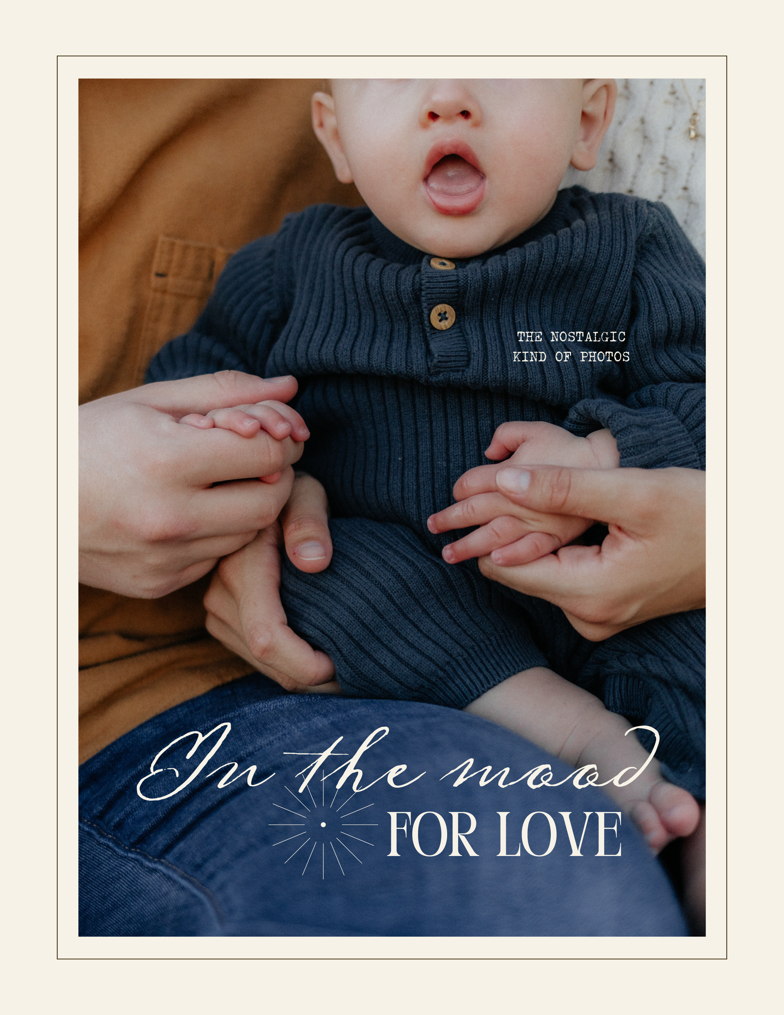 A baby wearing a navy ribbed sweater lies on brown fabric while adult hands hold their small hands.