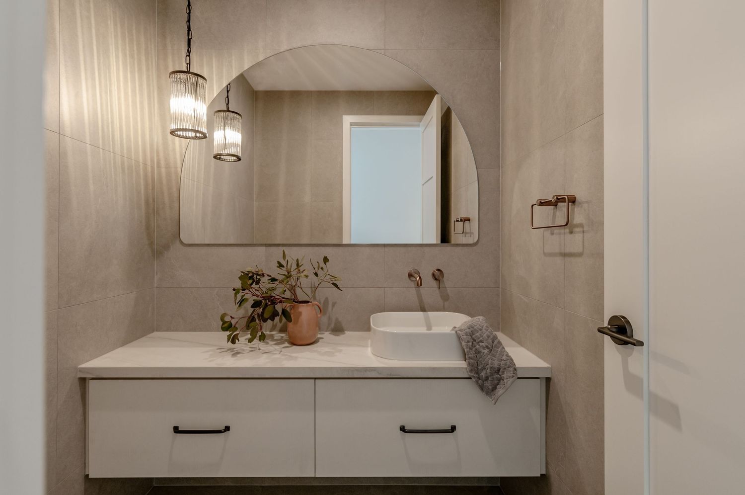 Modern bathroom interior with white walls, elegant pendant lighting, and floating vanity cabinets with dual sinks.