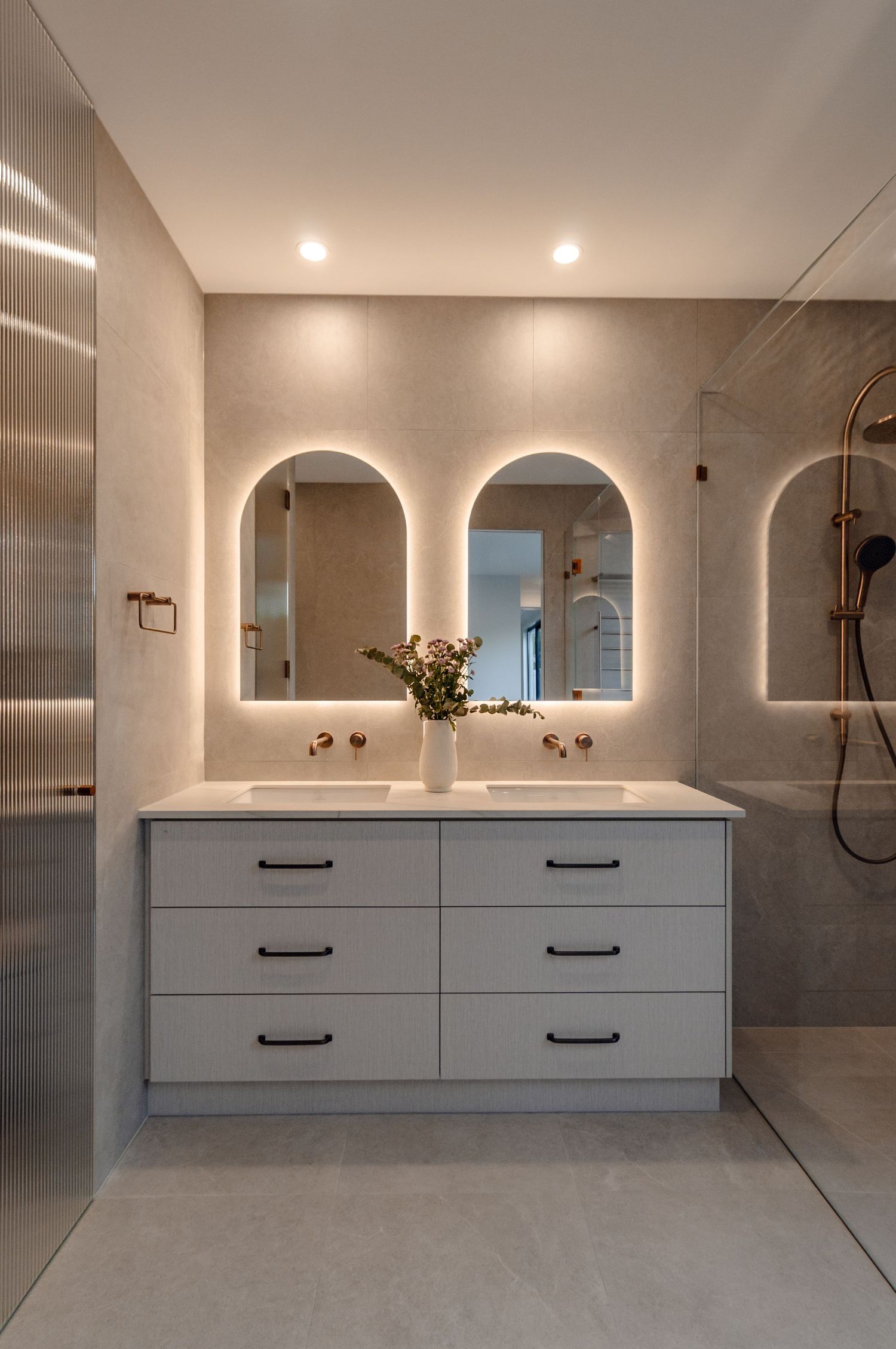 Modern bathroom vanity with white floating cabinets, dual circular mirrors, and backlit arches creating ambient lighting.