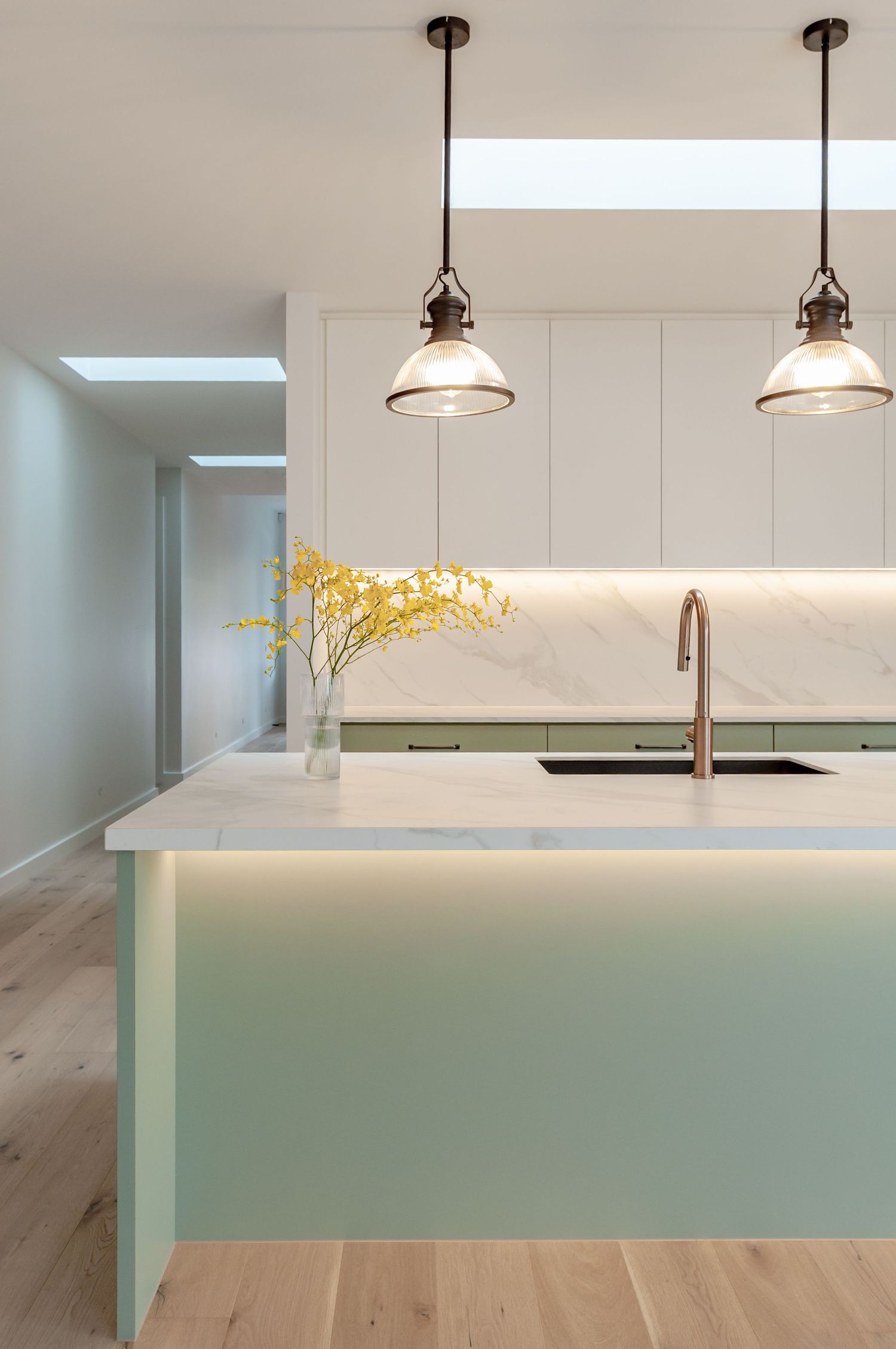Modern minimalist kitchen with white marble countertop island, pendant lights, and under-cabinet lighting features pale wood flooring.