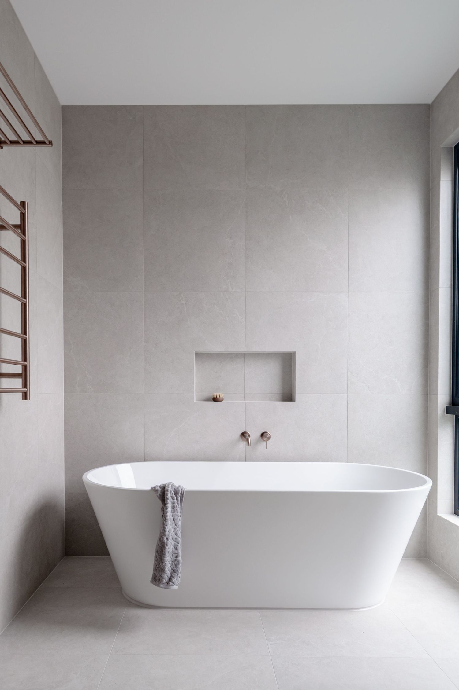 Modern minimalist bathroom featuring a freestanding white bathtub against light gray walls with a built-in wall niche and towel rack.