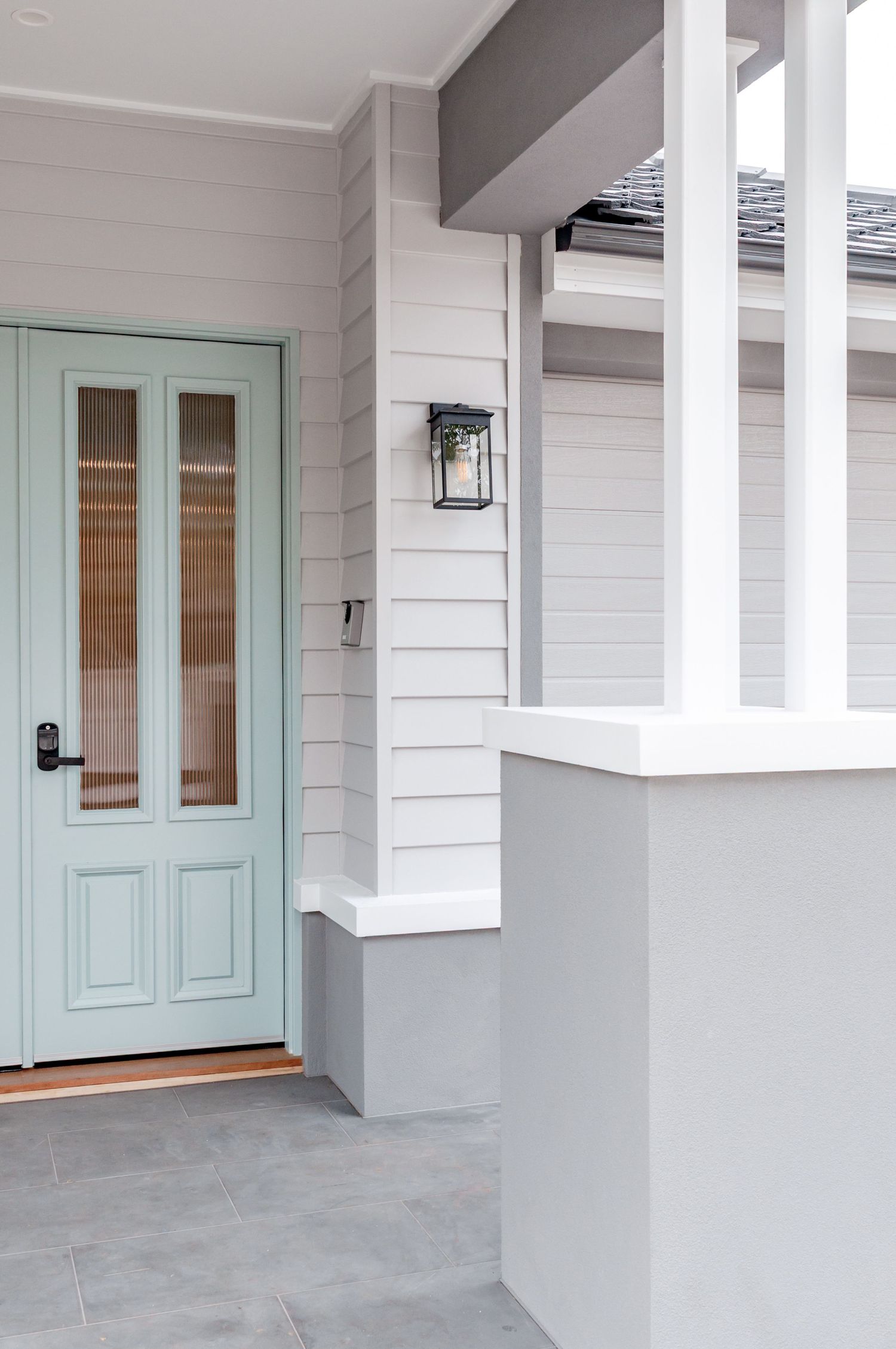 Modern coastal home entrance featuring a mint green front door with glass panels and white shiplap siding.