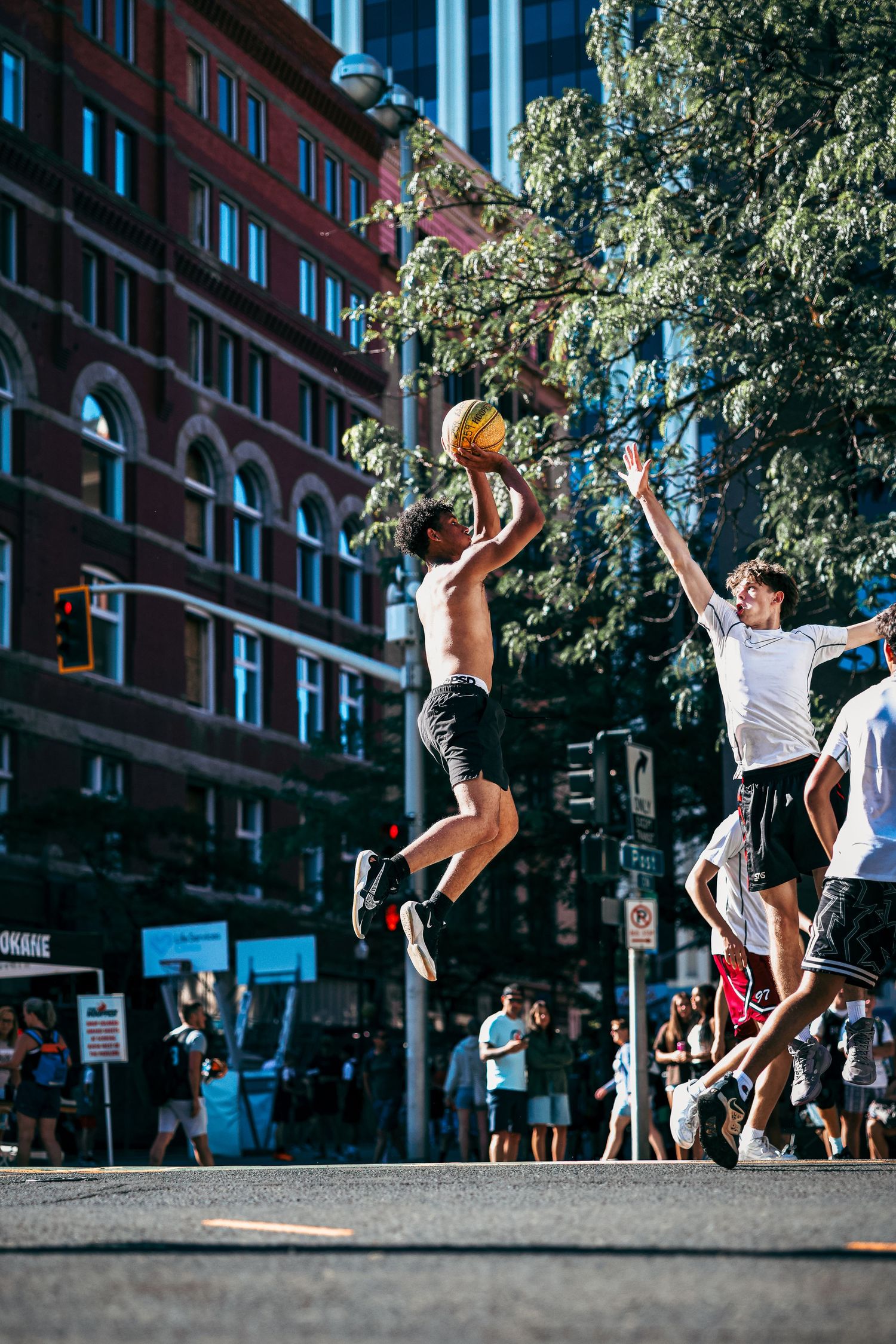 A sequence of basketball players jumping and dunking on an outdoor court in an urban setting with brick buildings.