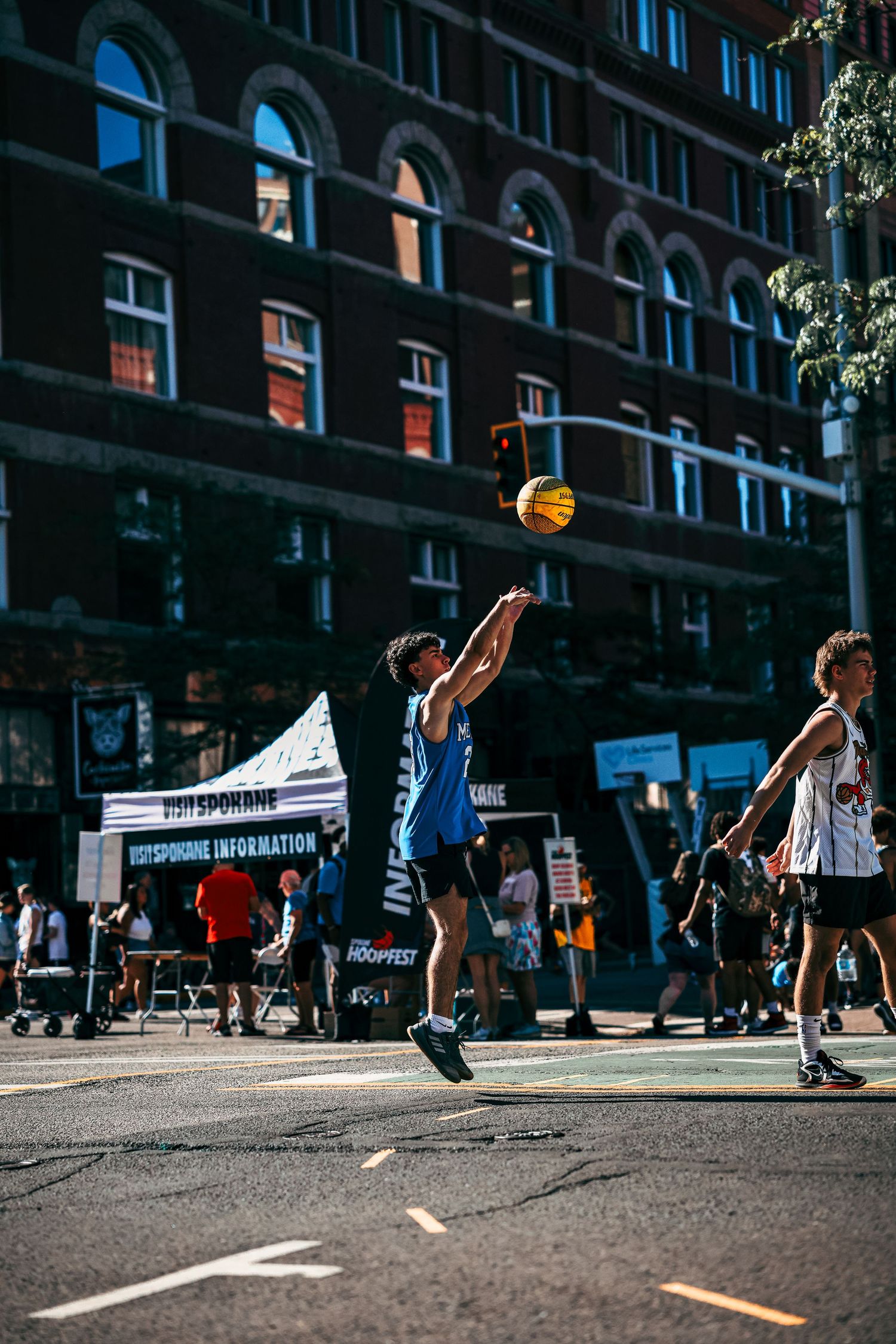 Basketball players engage in an intense street game on an urban court with buildings in the background.