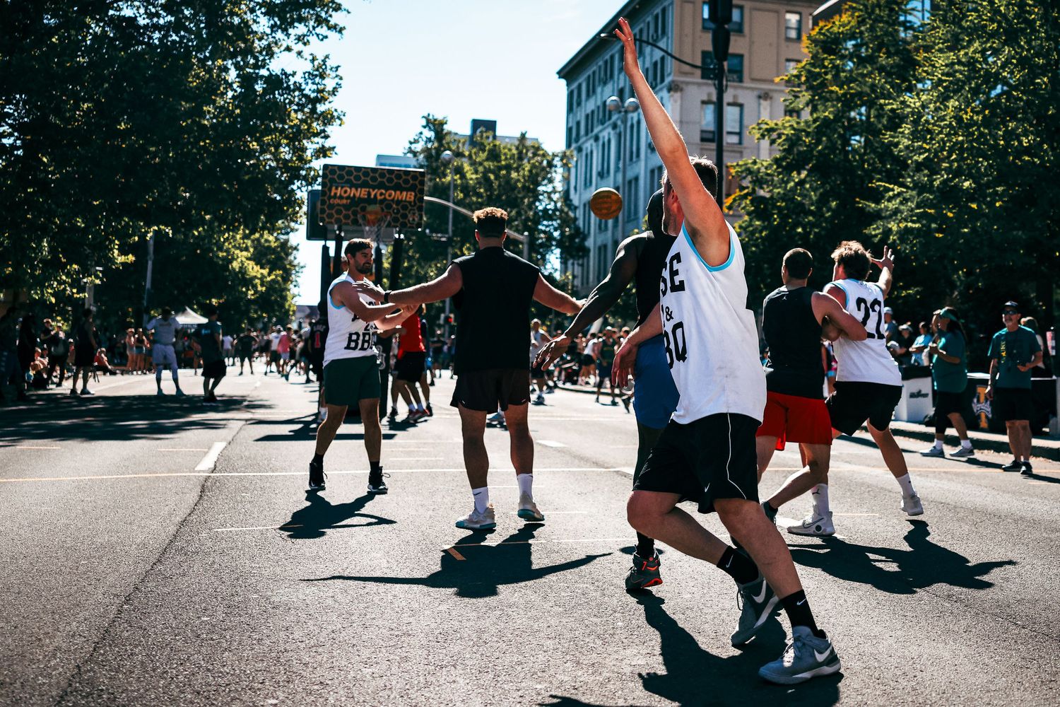 Basketball players compete in an intense street game on an outdoor court during a sunny day.