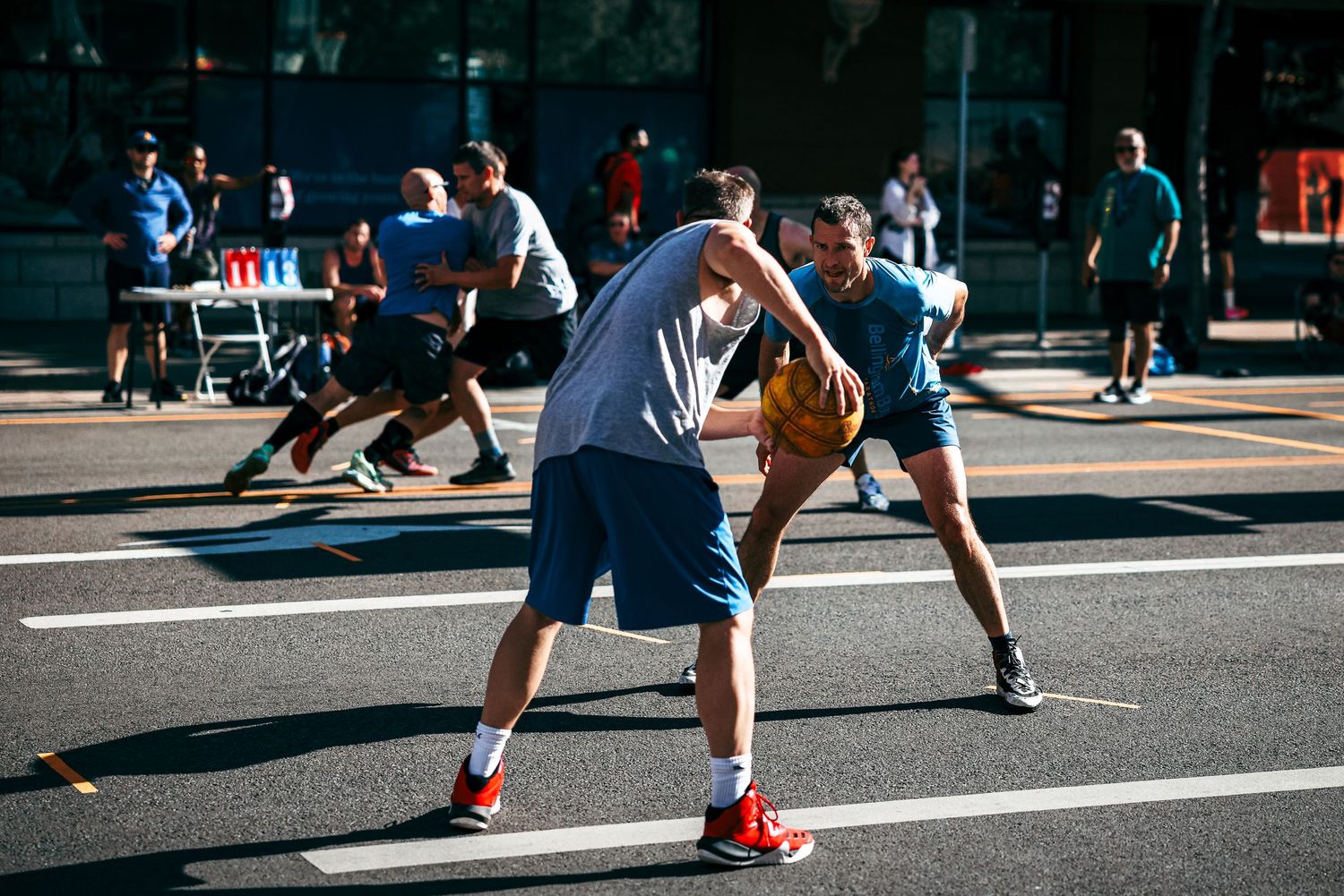 Basketball players dribble and play on an outdoor court during a sunny day street game.
