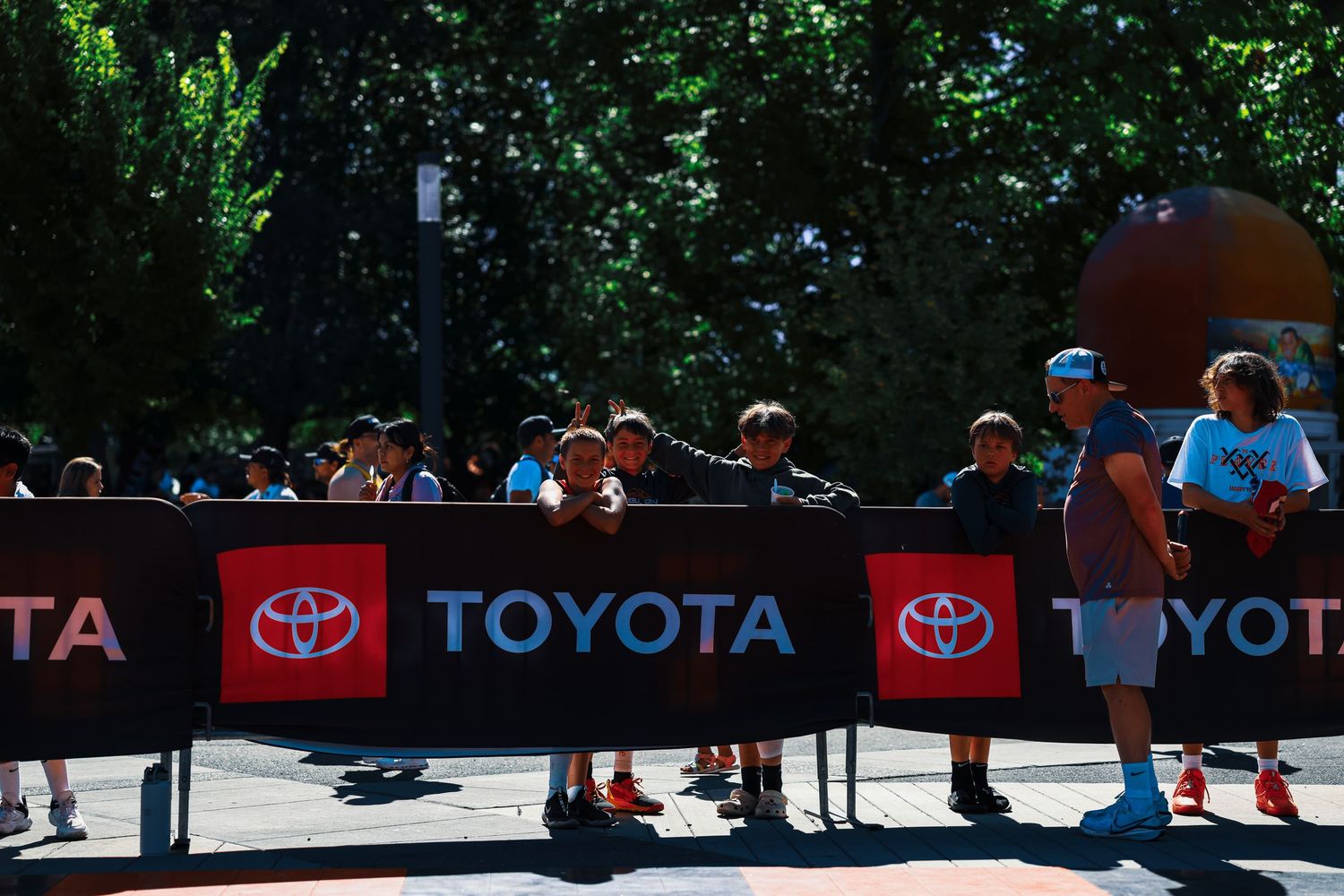 Athletes compete in a cycling event with spectators watching along a tree-lined course with Toyota banners visible.
