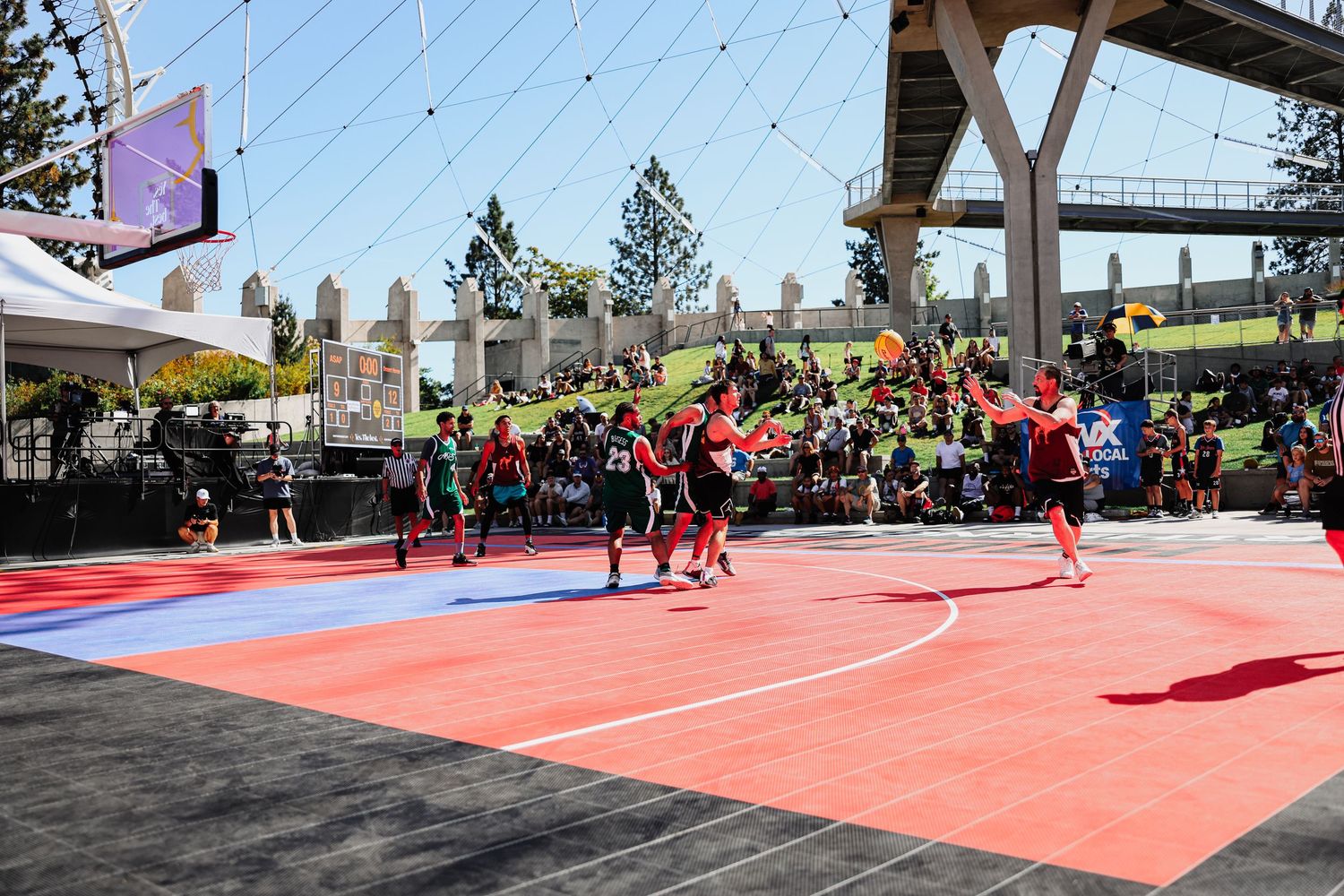 Athletes compete in a martial arts tournament on red mats under an outdoor canopy structure.