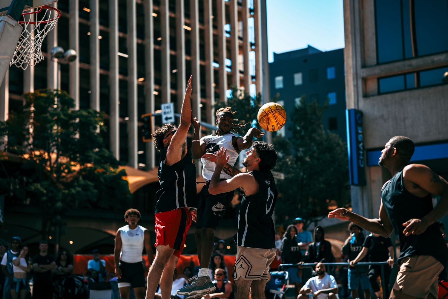 Basketball players compete in a street game during a summer tournament in an urban setting.