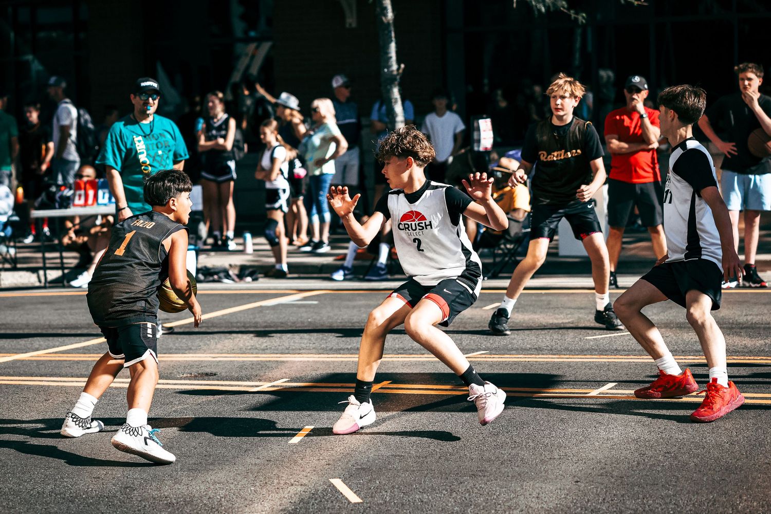 Basketball players in athletic gear perform defensive slide drills on an outdoor court during practice.