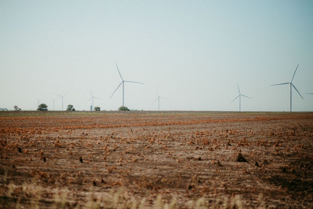 Wind turbines stand on a vast arid landscape against a pale blue sky in a rural setting.