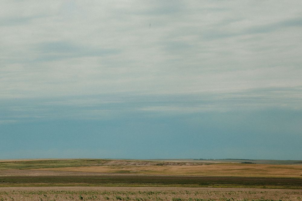 Rolling prairie grasslands stretch toward the horizon under a cloudy blue sky in rural America.