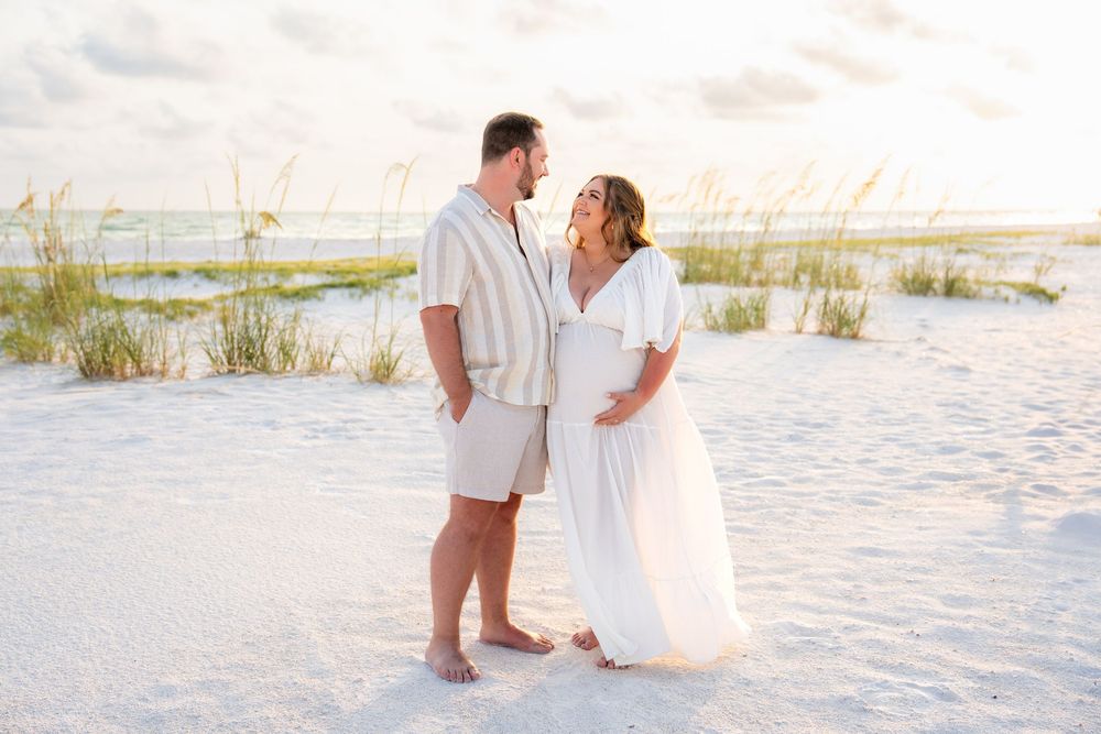 Expecting couple sharing a tender moment on a white sand beach at dusk.