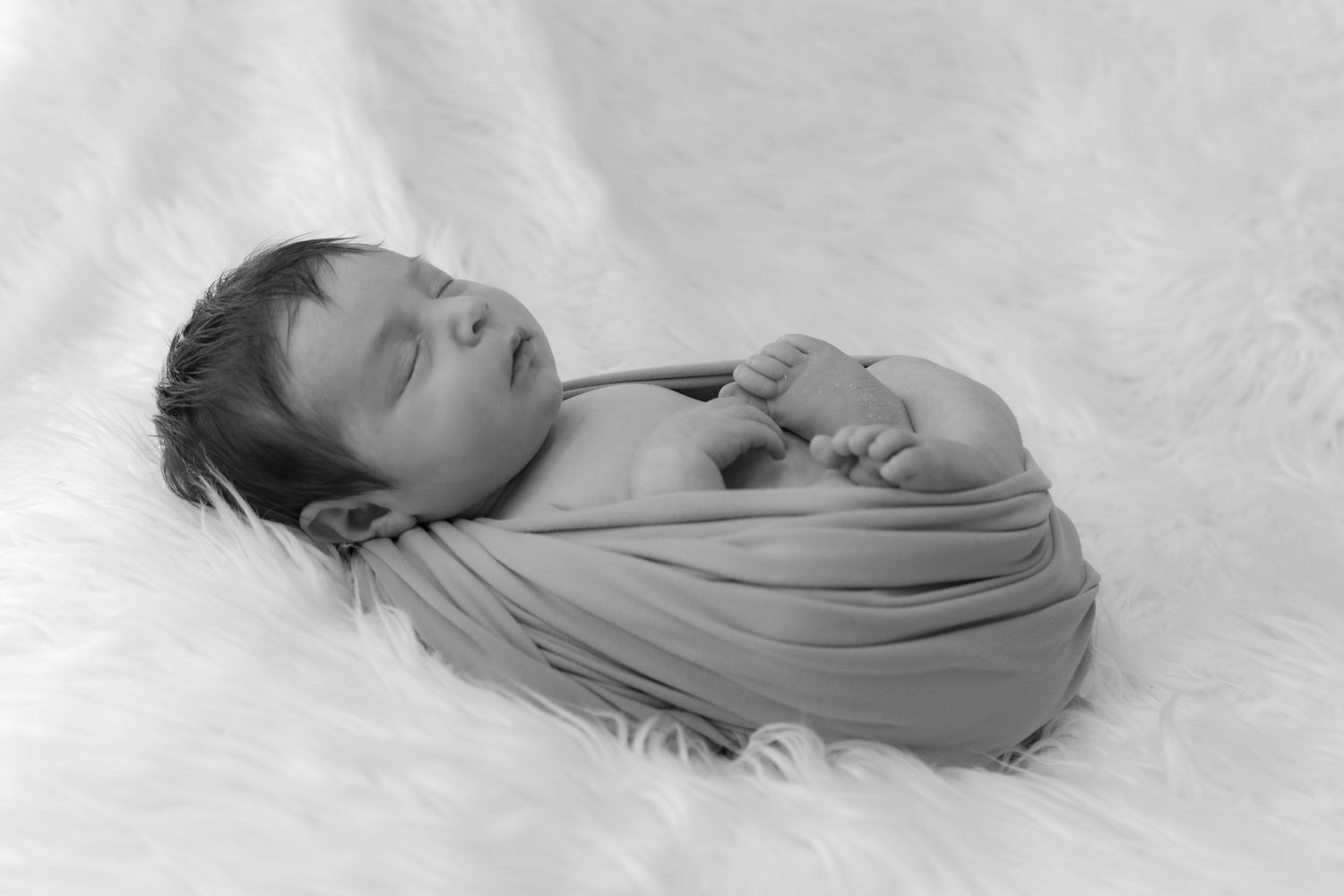 Black and white photograph of caring hands gently cradling a newborn baby lying on a soft blanket.