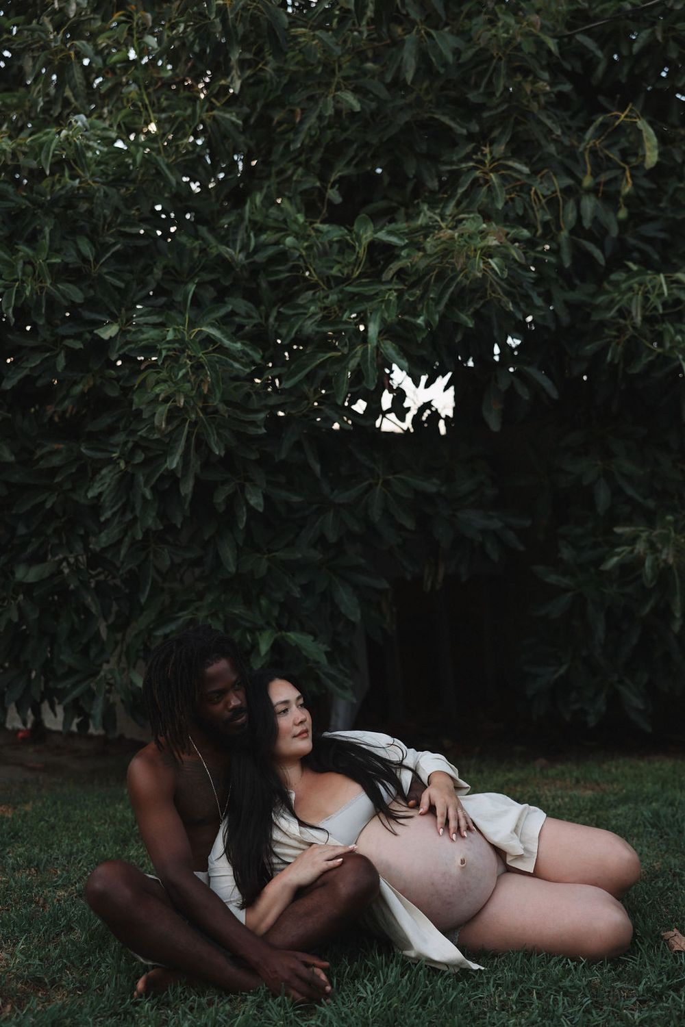 Woman in nature lying on grass surrounded by dark green foliage in artistic outdoor photography.