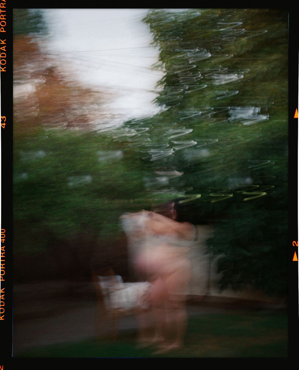 Abstract motion blur photograph captures pink and green hues through raindrops on window glass creating dreamy effect.