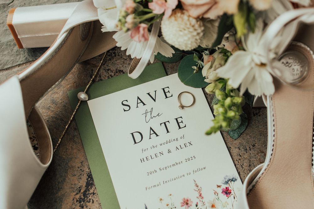 Wedding invitation suite with pink and white flowers arranged on a light wooden surface with save the date cards.