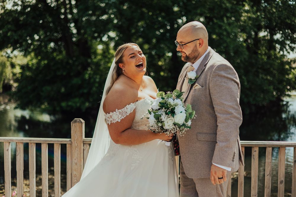 A joyous moment captured between newlyweds on a wooden bridge, with the bride holding a blue and white bouquet.