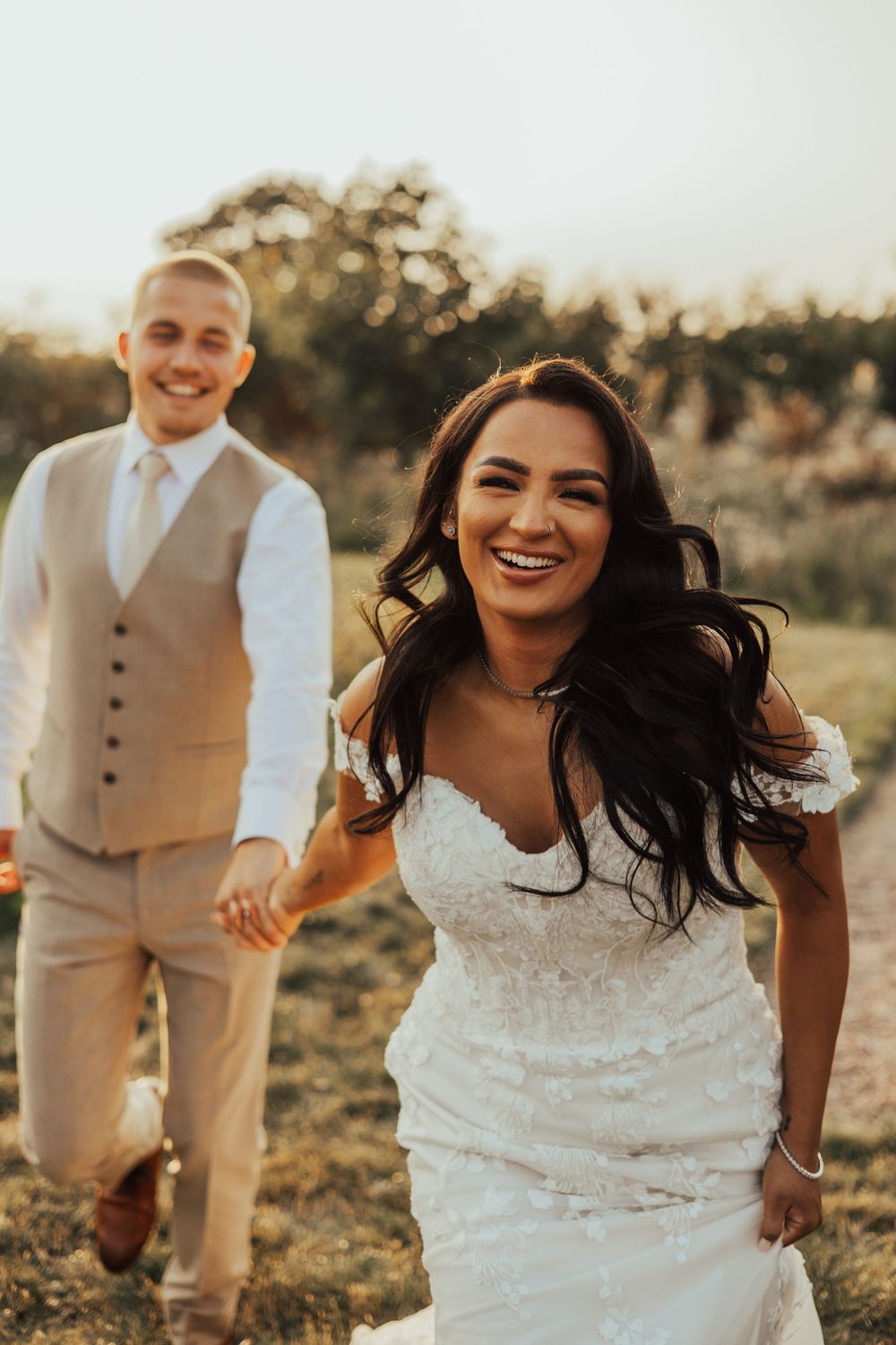 A couple shares joyful moments during their wedding photoshoot in a sunlit outdoor field at golden hour.
