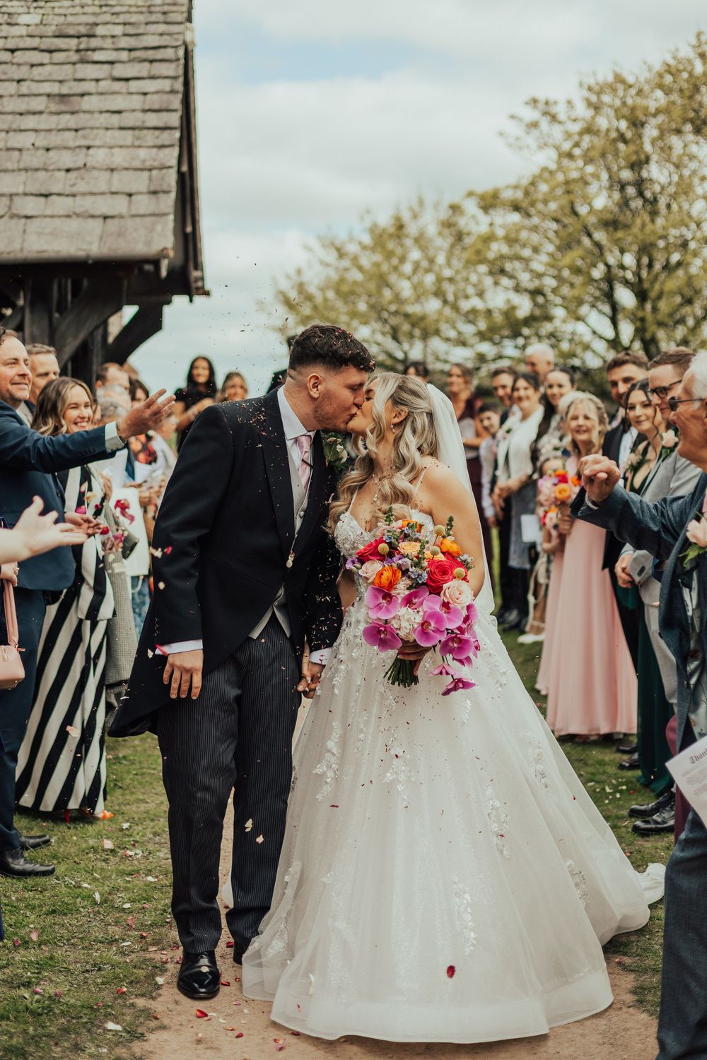 Bride and groom kissing during confetti throw outside rustic barn wedding venue.