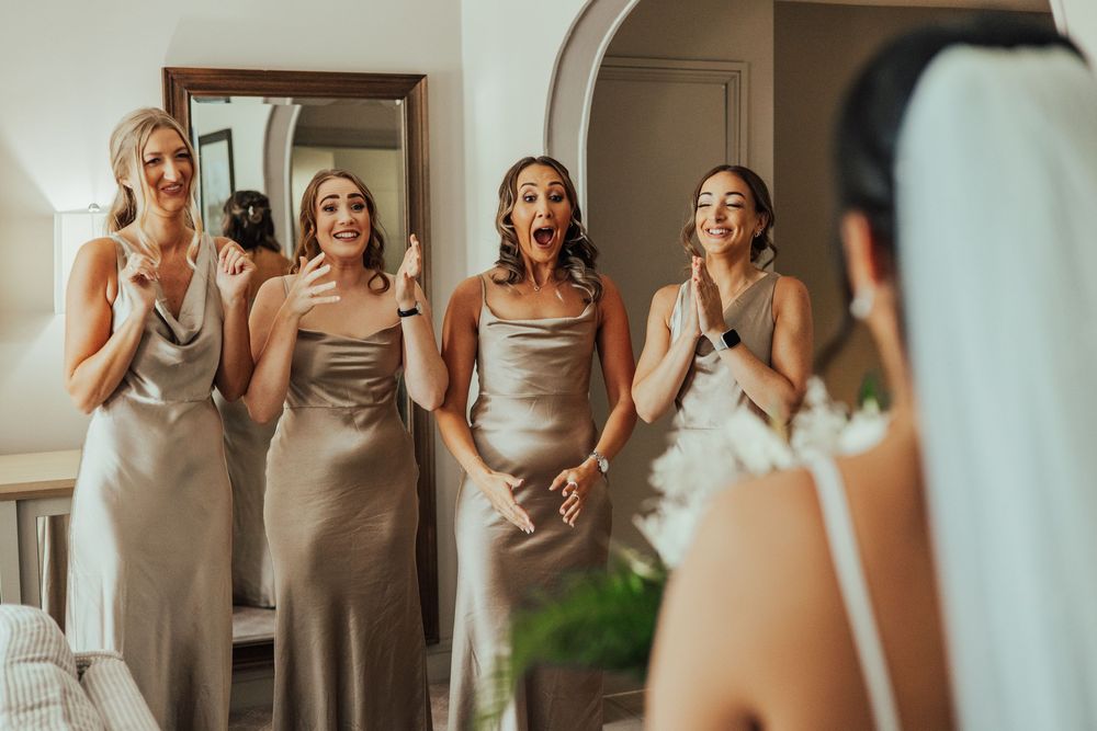 A wedding party reacts with excitement and joy while getting ready in a bridal suite.