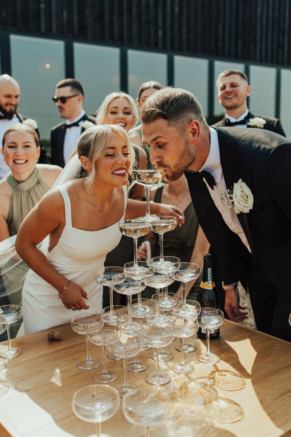 Wedding couple sharing a joyful moment while sipping from a champagne tower at their reception celebration.
