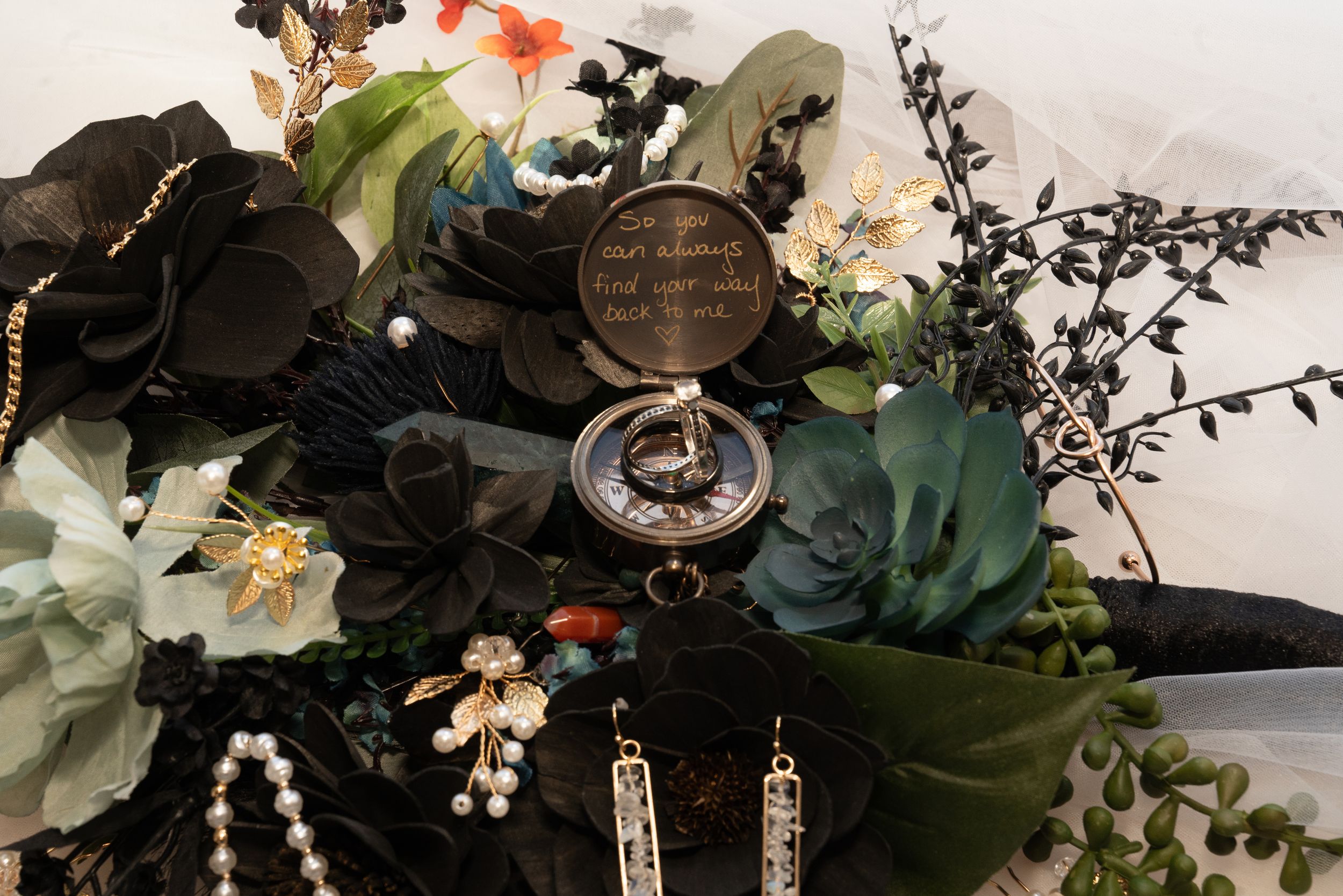 Vintage compass surrounded by black and white flowers, pearls, and greenery on a white background.