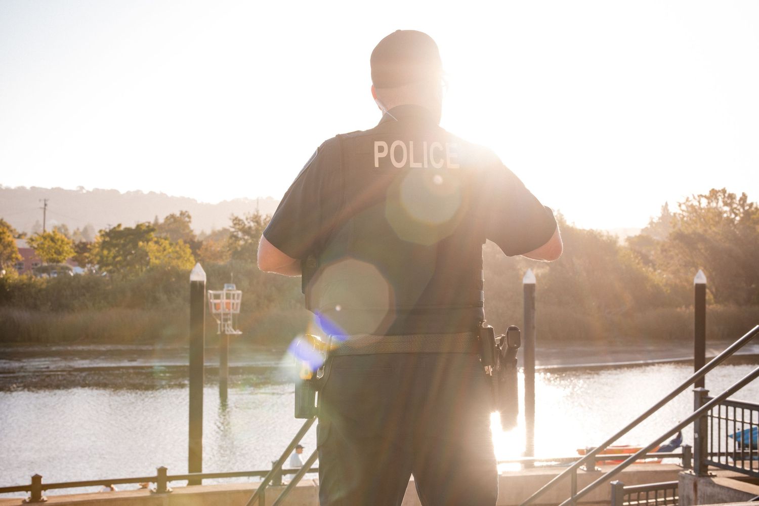 Police officer patrolling waterfront area during golden hour sunrise.