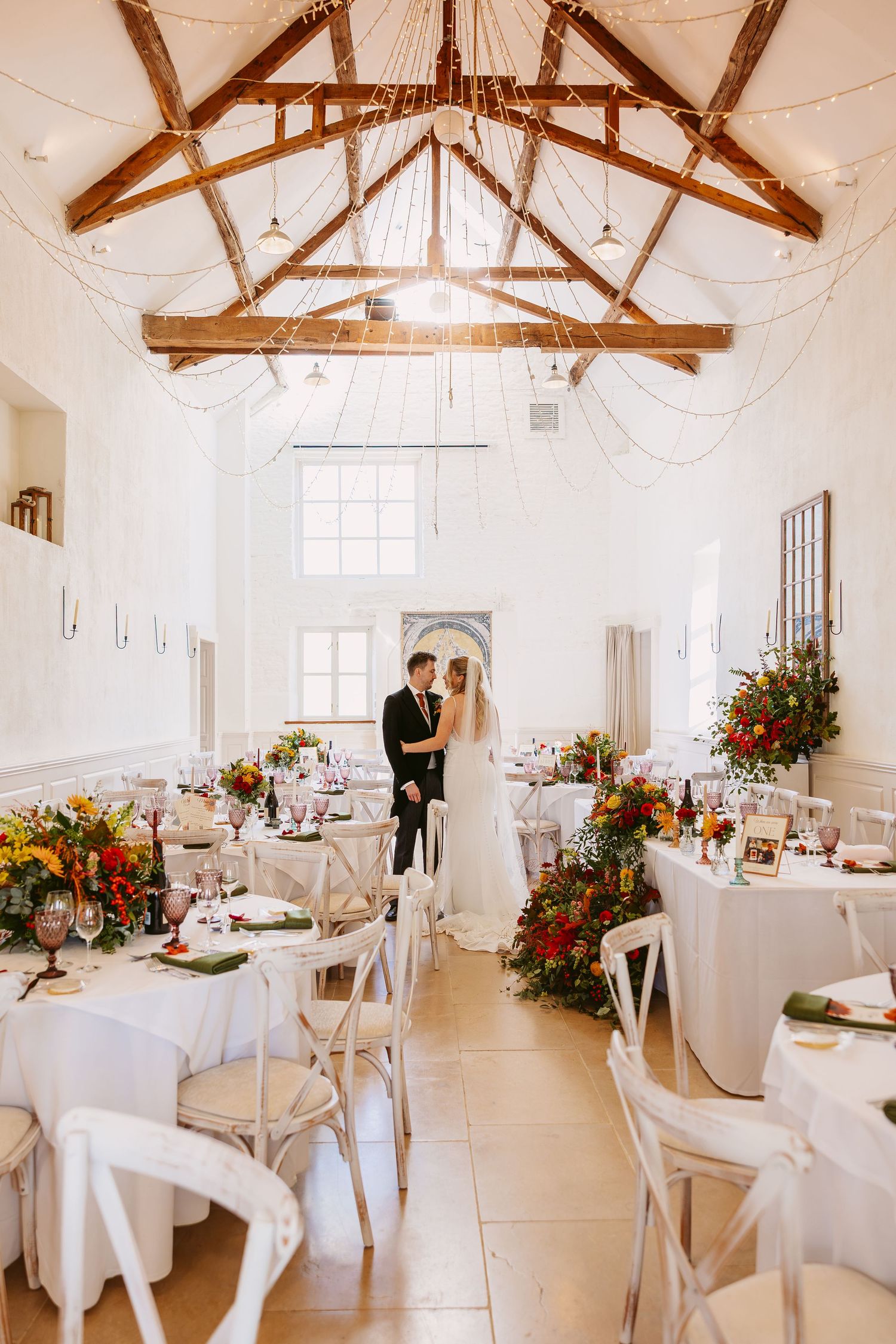 Merriscourt White barn elegant wedding venue interior with exposed brick walls, white draping, floral chandeliers and white chiavari chairs.