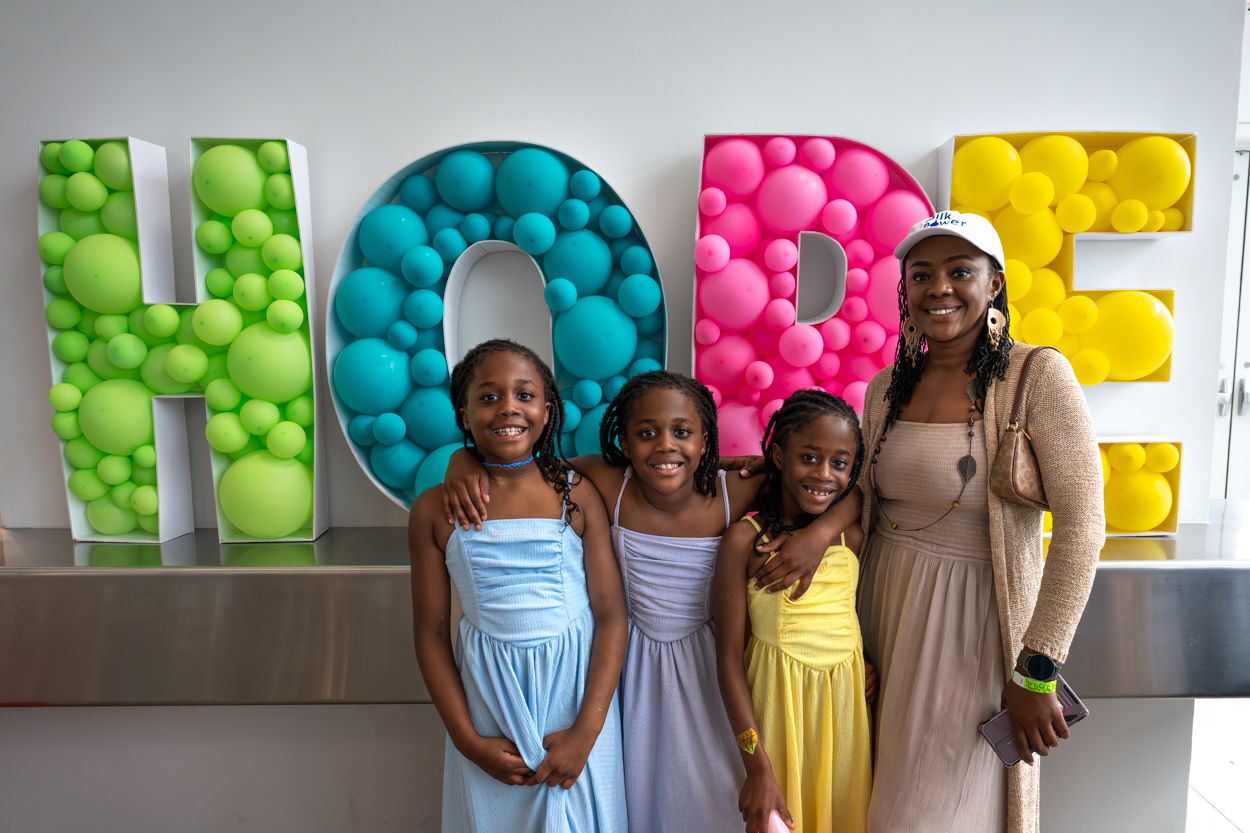 Four girls smiling in front of a colorful HOPE balloon letter display at an indoor event.
