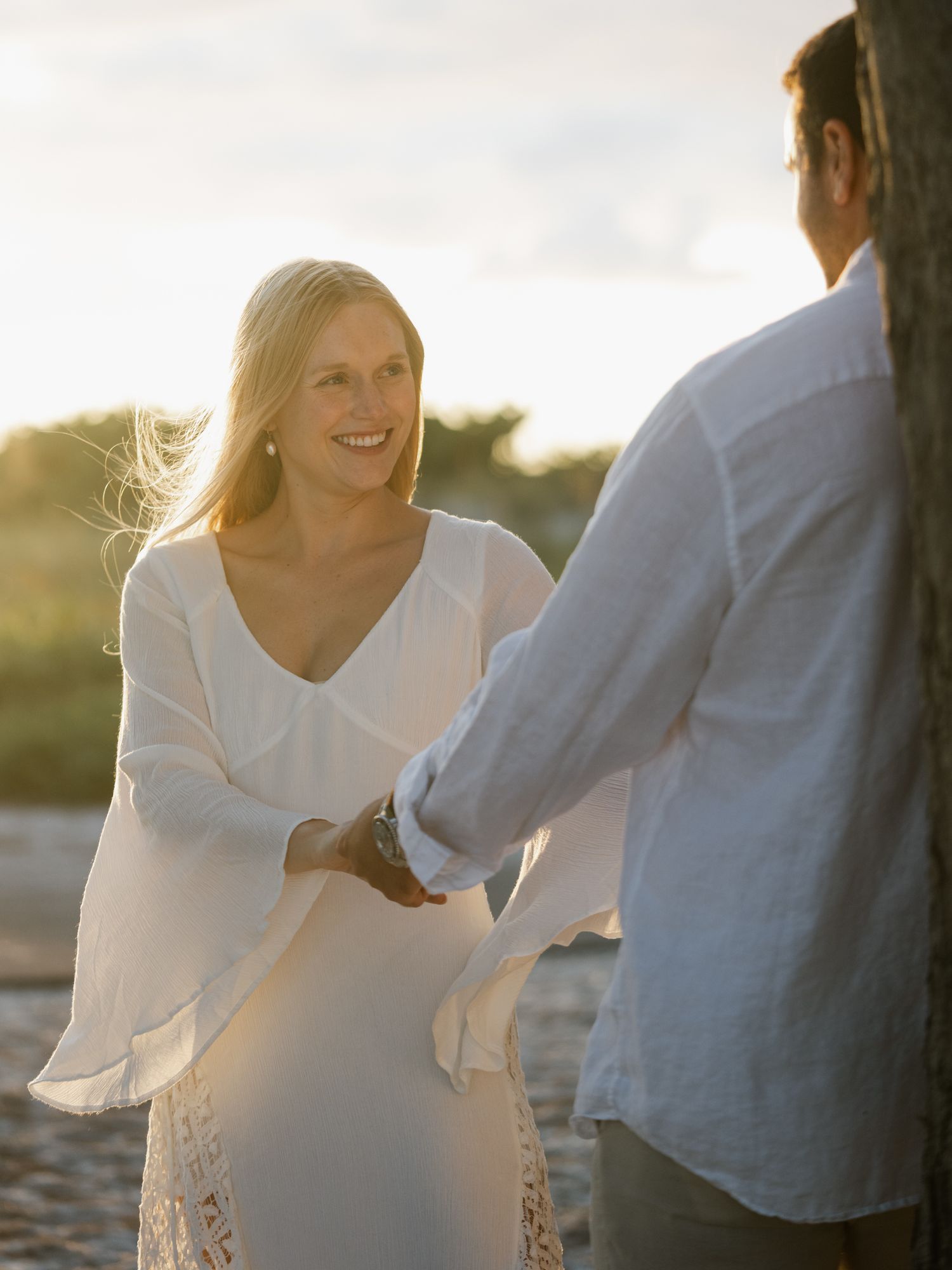 Couple in white clothing sharing tender moments on a beach during golden hour.