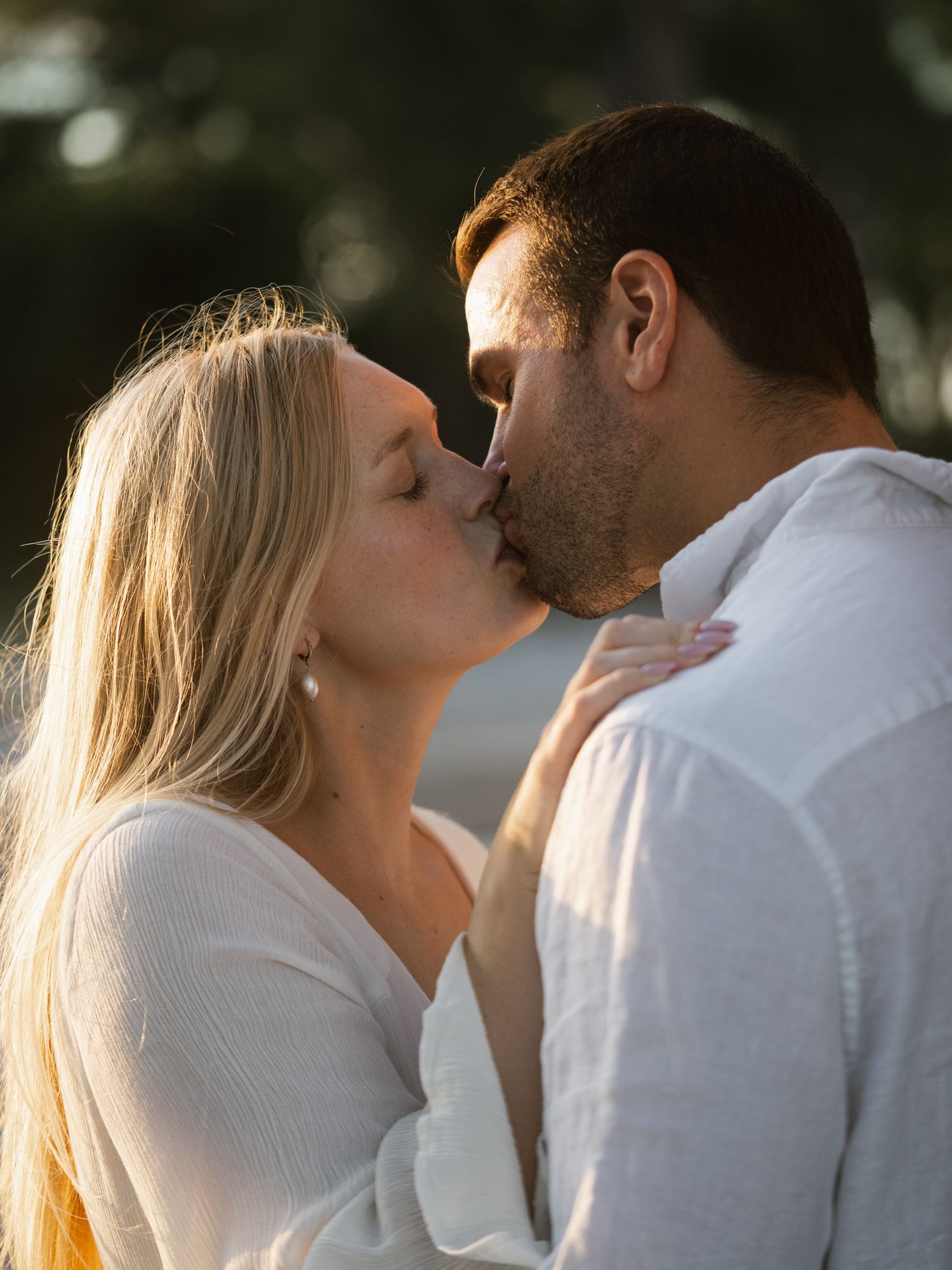 Romantic couple in white clothing sharing an intimate moment outdoors.