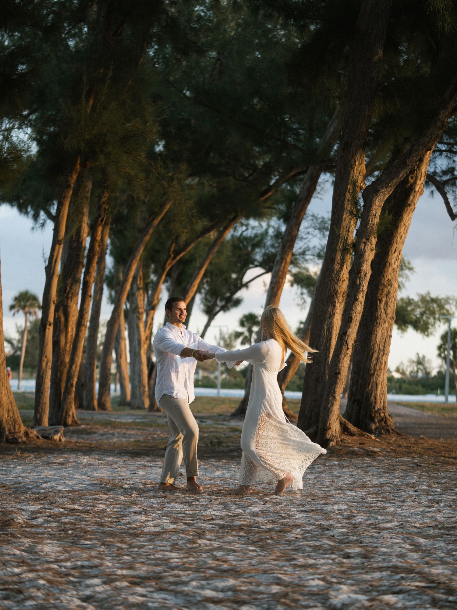 Playful couple dancing among a row of tall pine trees.